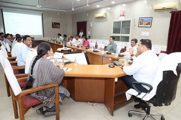 सम्मेलन कक्ष में मेज के चारों ओर बैठे अधिकारी बैठक करते हुए
