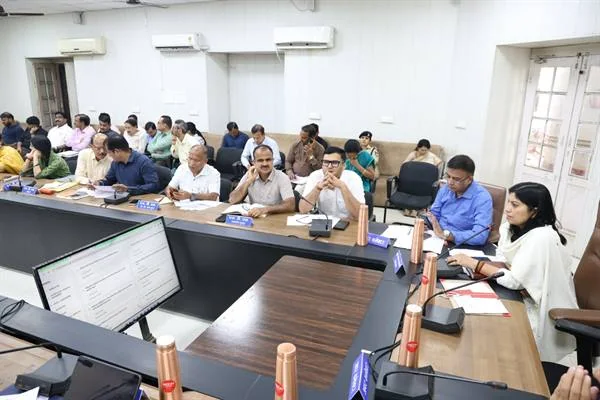 सभाकक्ष में लंबी मेज के चारों ओर बैठे अधिकारी बैठक करते हुए